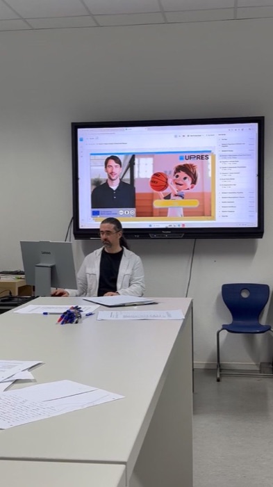 A trainer at a desk with a UP-RES module playing on the screen behind.