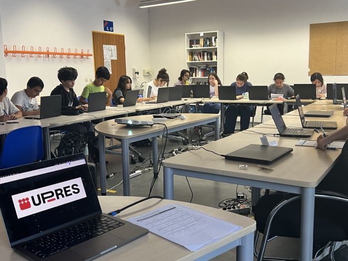 Students at laptops in a computer room, with the UP-RES logo on the screen in the foreground.